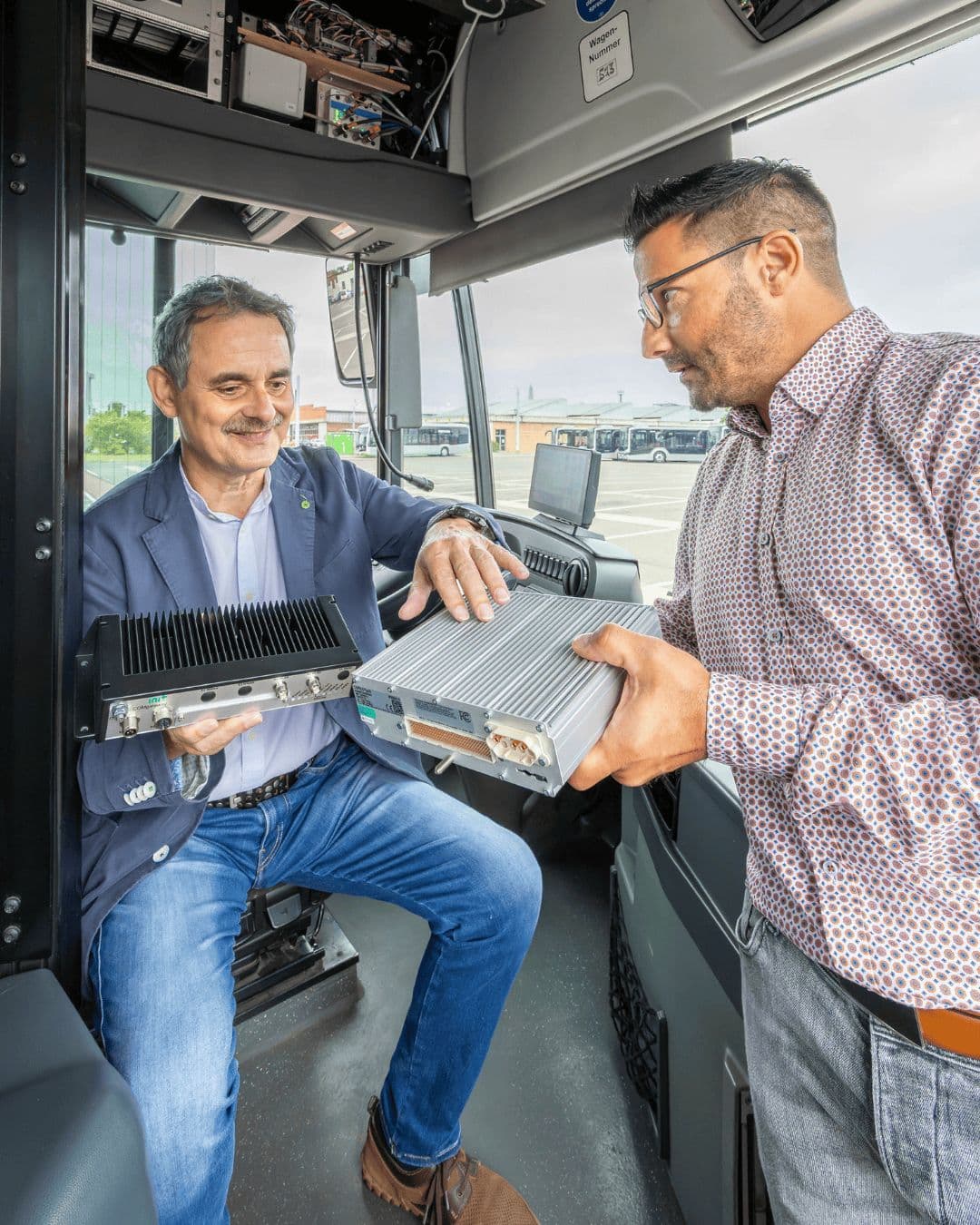 Peter Kolbert (Stadtwerke Halle) und Andreas Blümner (Stadt Halle) im Austausch über die neue Bordtechnik, den schwarzen "Com Gateway" und den silbernen Bordrechner. Foto: Stadtfotograf Thomas Ziegler
