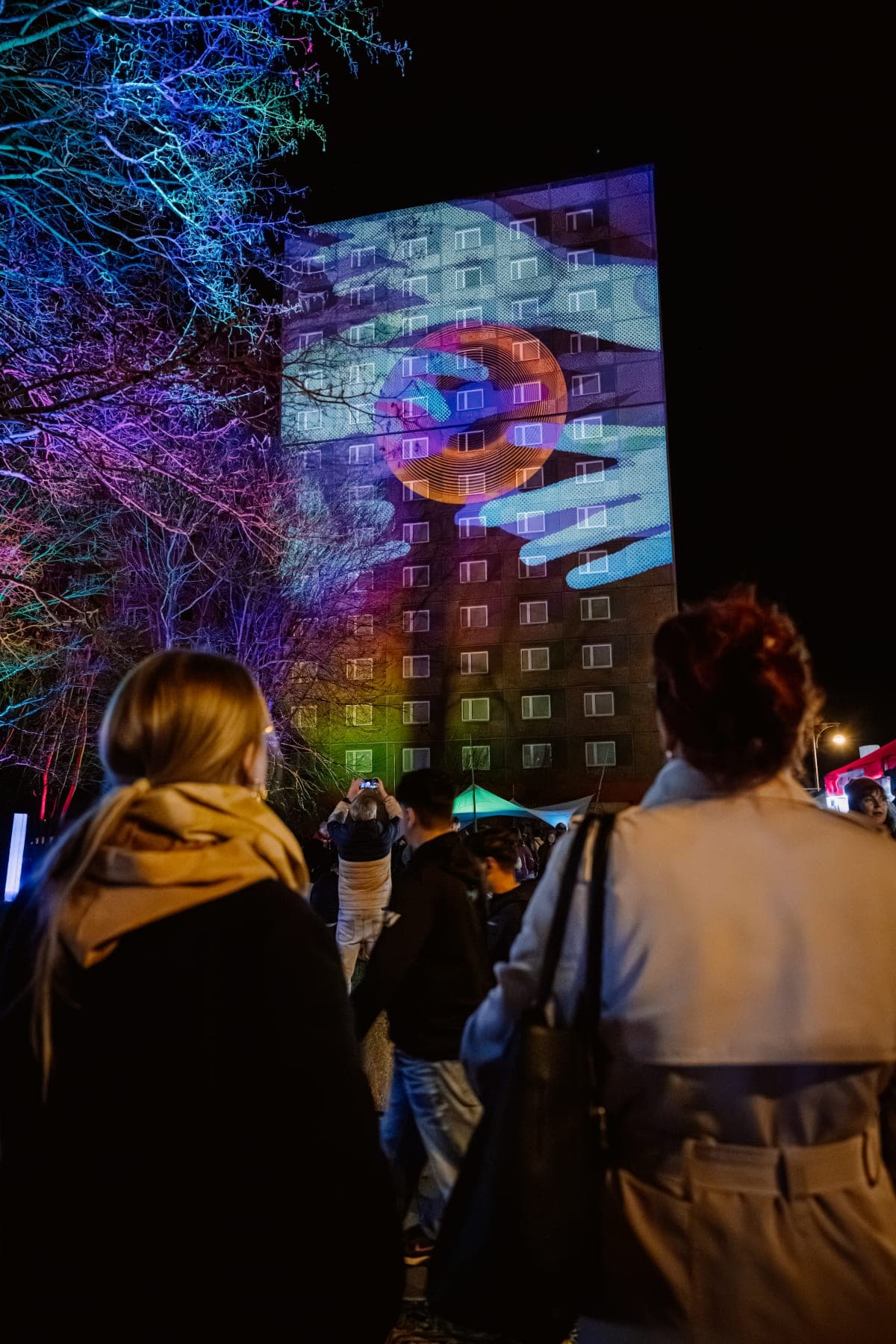 Menschen bestaunen eine große Fassadenprojektion in Halle-Neustadt; Fotografin Anna Kolata
